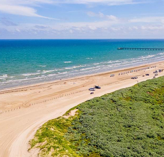Aerial view of Port Aransas Beach with clear blue water, sandy shores, and a nearby pier