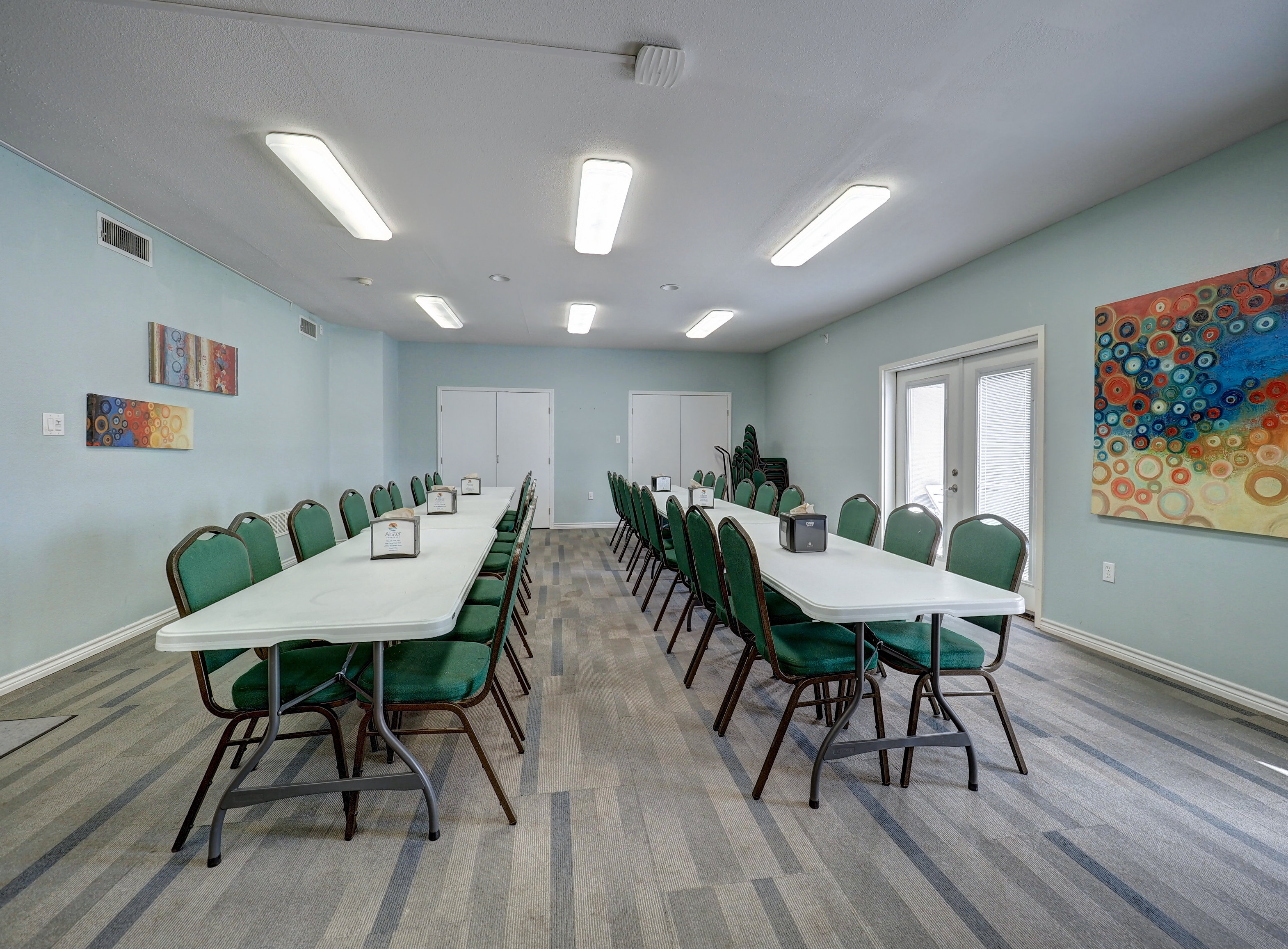 A meeting room with long tables and green chairs.