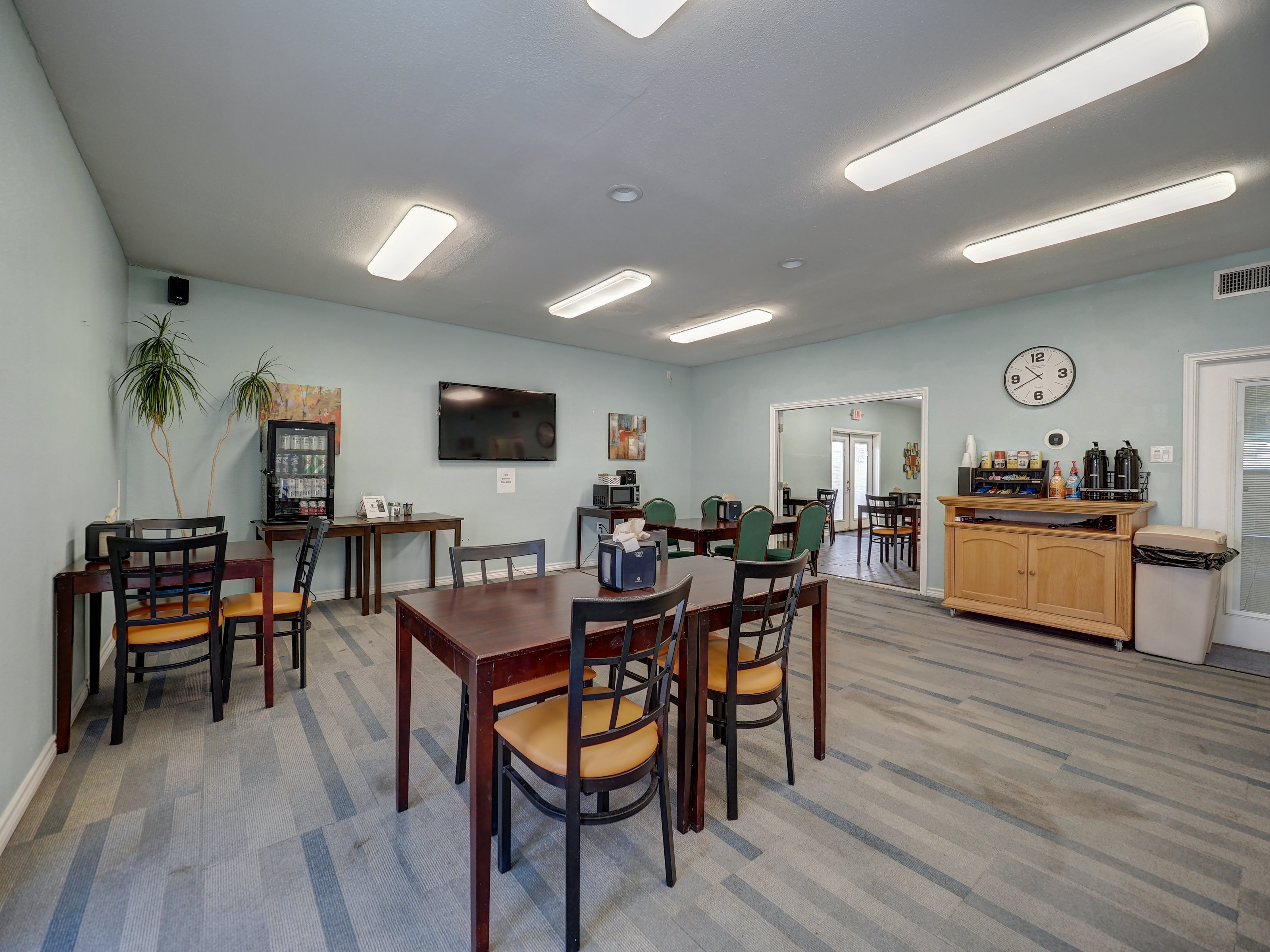 A hotel lobby with tables, chairs, a TV, and a coffee station.