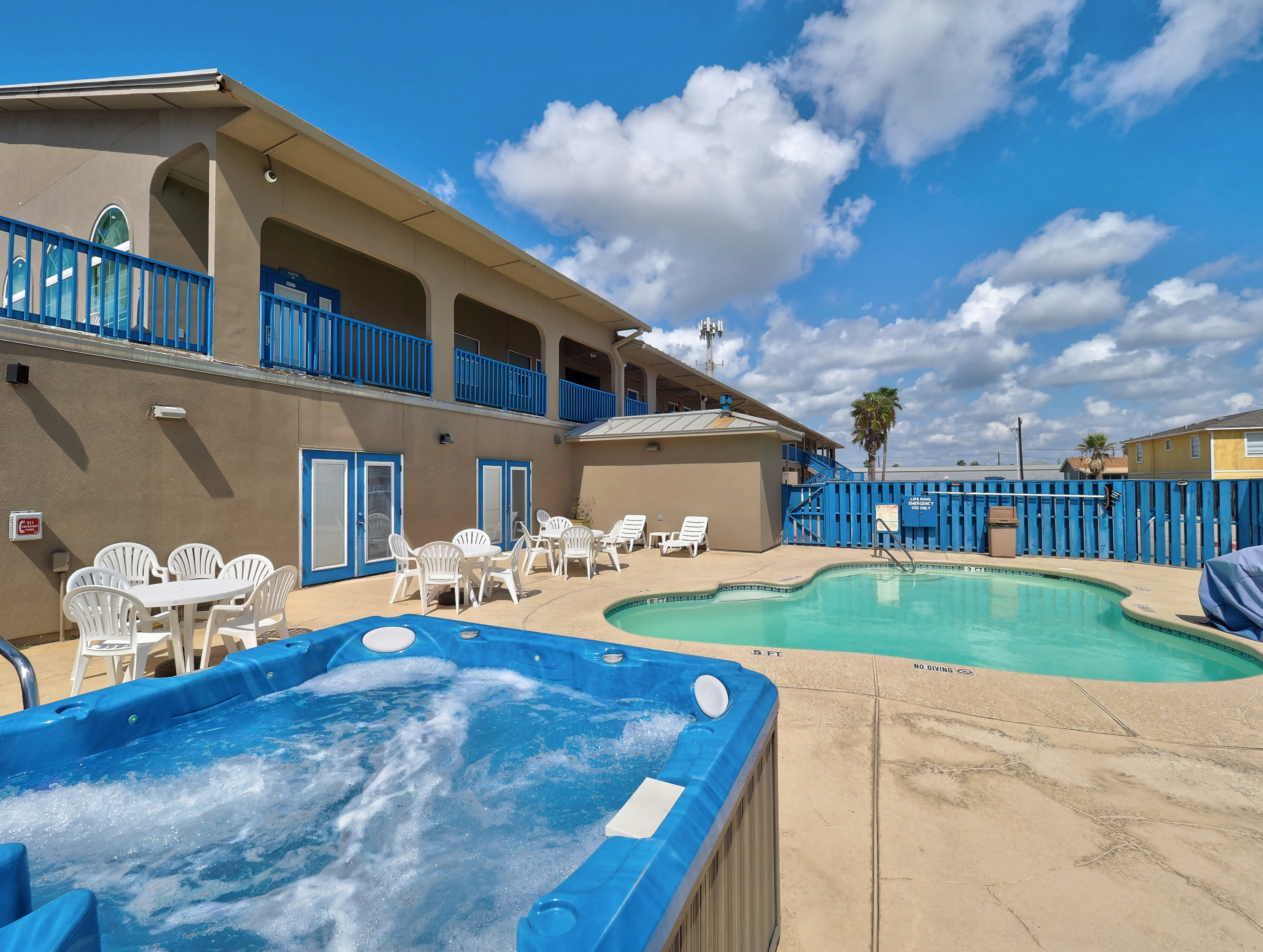 A hotel exterior with a pool and hot tub on a sunny day.