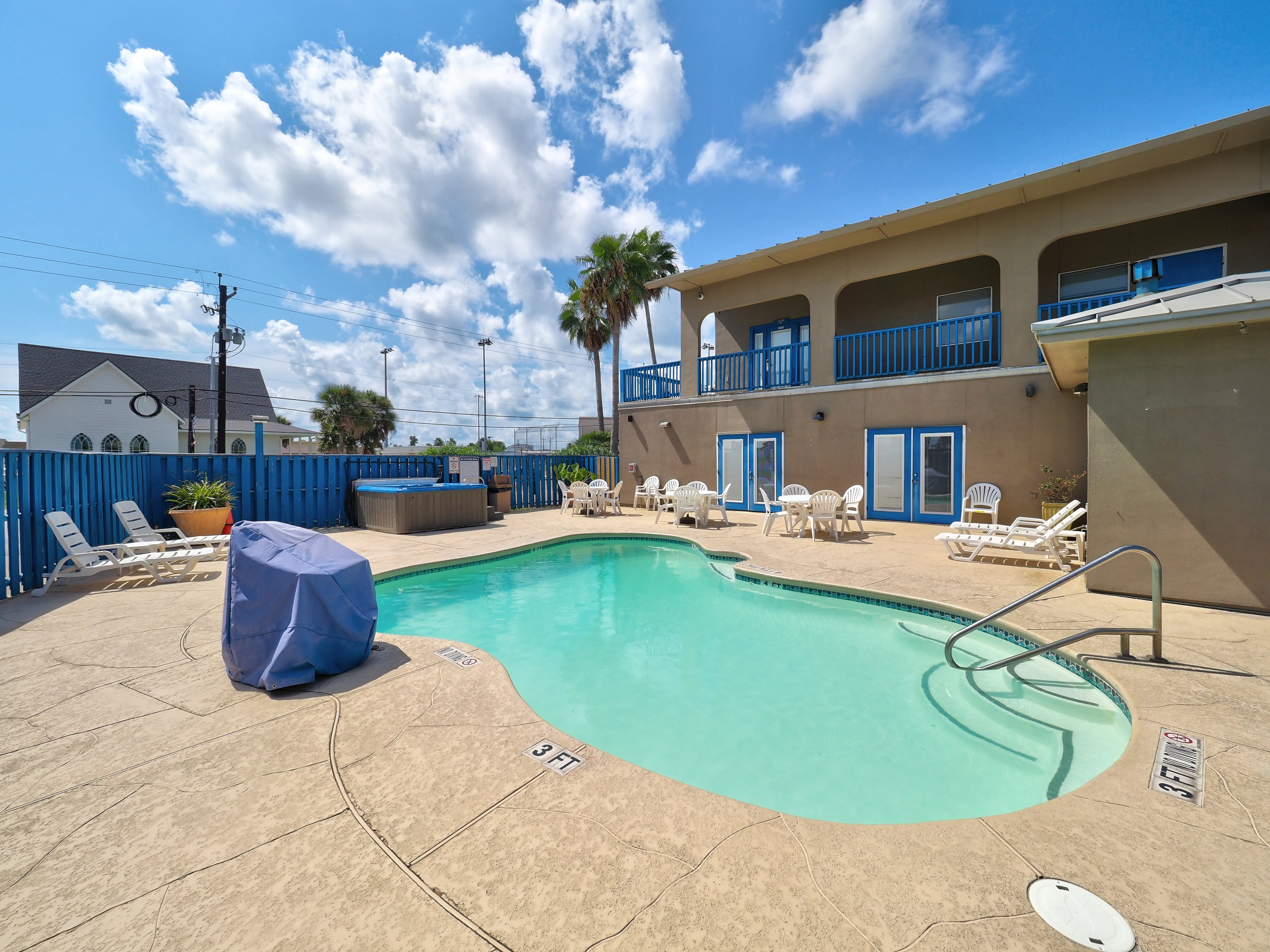 A pool area with a pool, hot tub, and balcony on a sunny day.