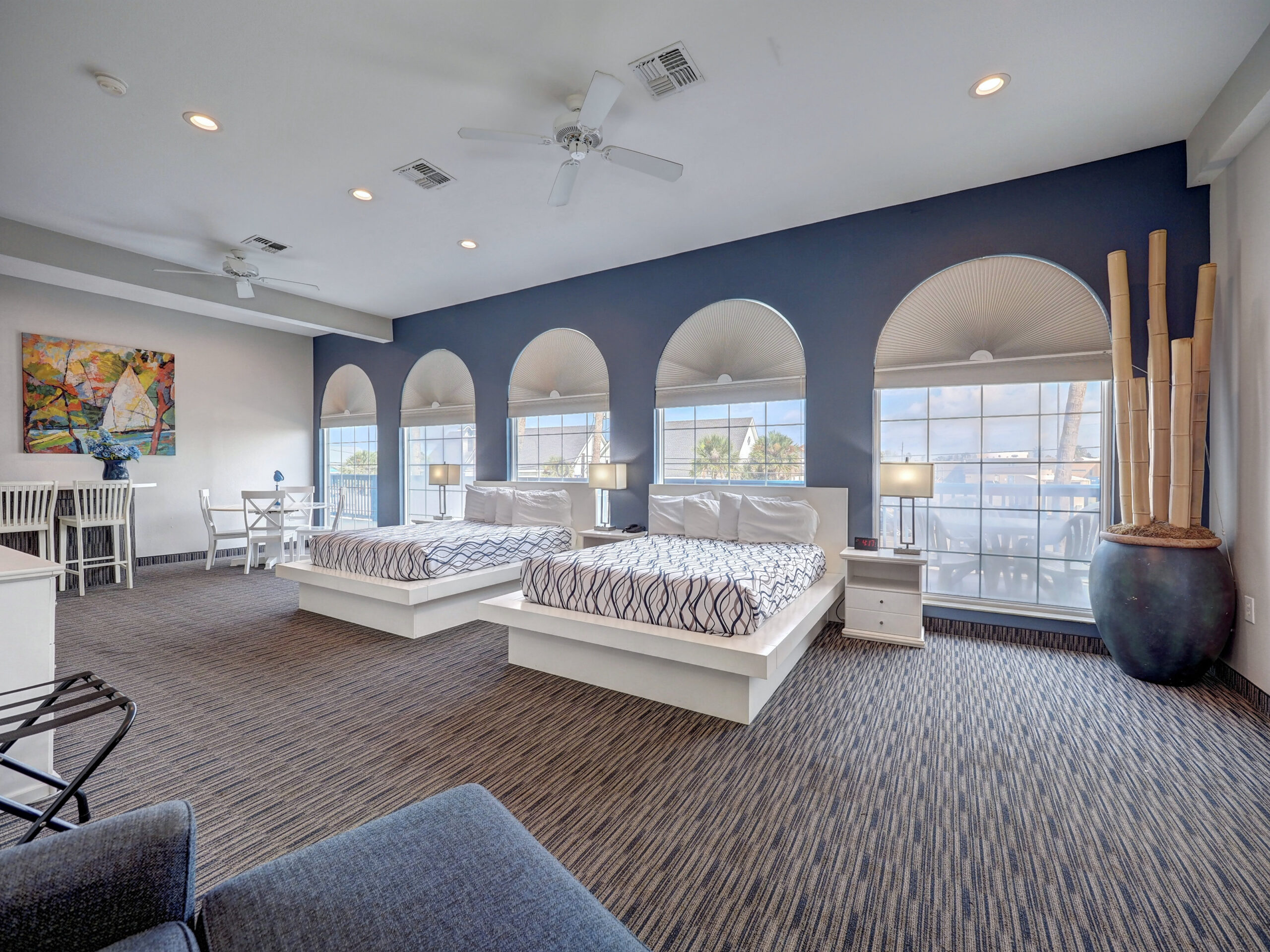 A wide room with two queen beds, a dining table, a sofa, and large arched windows.
