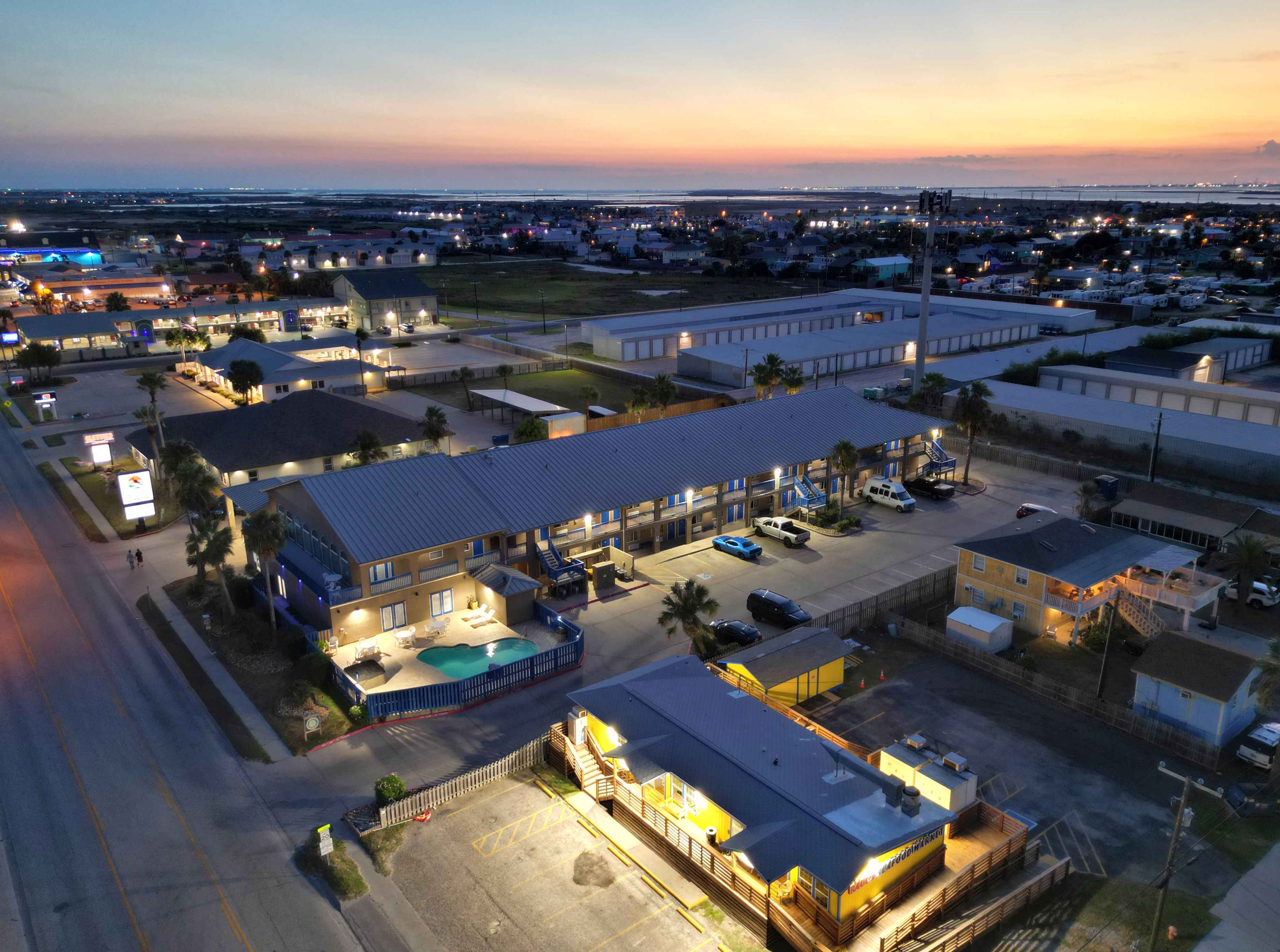 Aerial view of a hotel at dusk with a pool and parking lot.